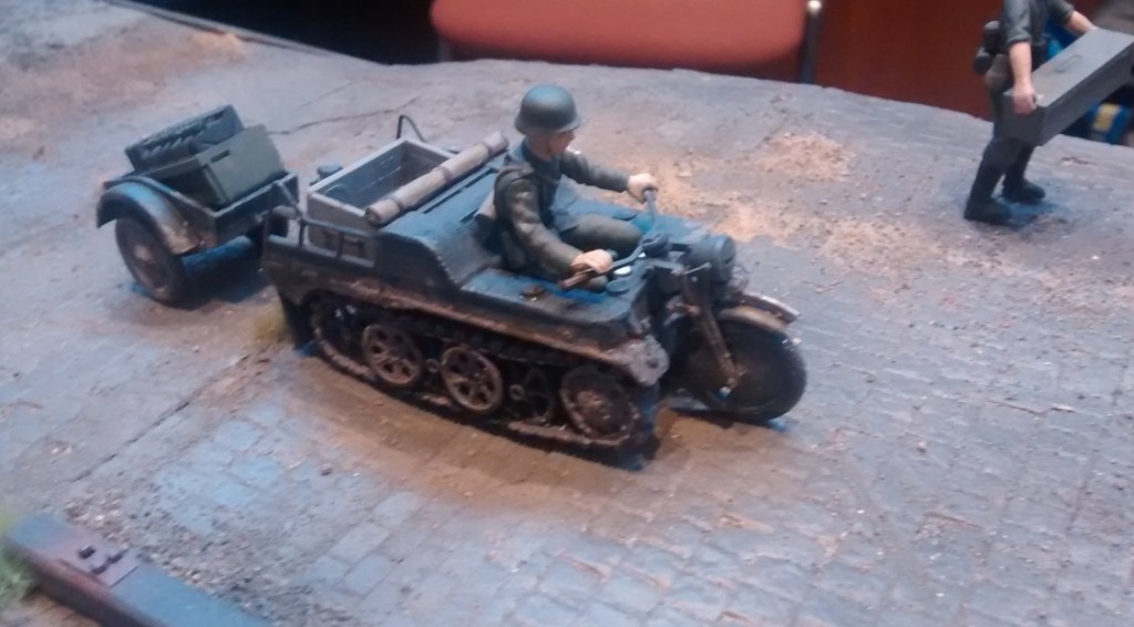 Ein Melder fährt in seinem Sonderkraftfahrzeug Sd.Kfz. 2 / Kleines Kettenkraftrad Typ HK 101 über die Laderampe, während die Granaten des gerät 040 verladen werden.