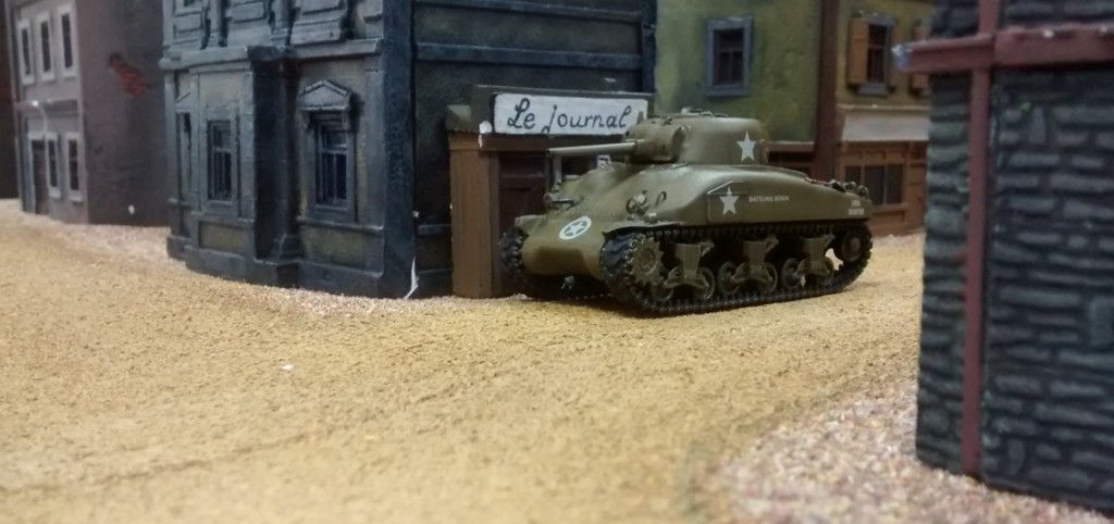 Der M4A1 Sherman hat die Straßenkreuzung im Ort erreicht. Er zieht ganz dicht an die eine Häuserwand, um nicht ein größeres Ziel abzugeben als nötig. Die Zeitungen sind leider nicht aktuell...