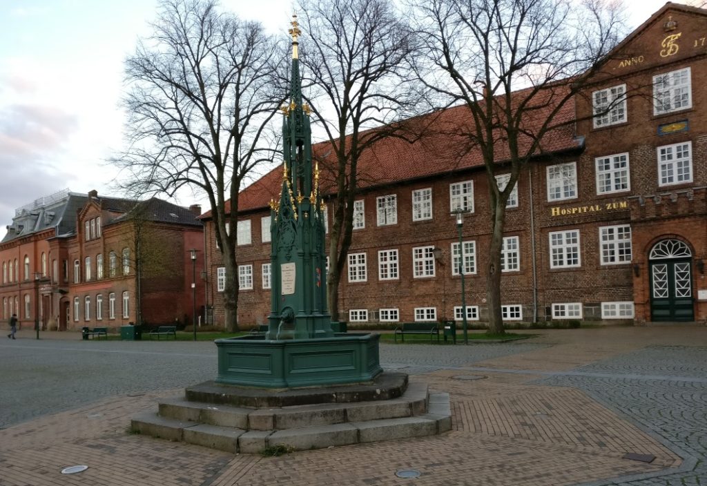 Davor: der Brunnen auf dem Schlossplatz mit der Inschrift: „Graf Gerhard der Grosse bestätigt und erweitert der Stadt Rendsburg Gerechtsame und Gebiet am Nicolaitage 1339“