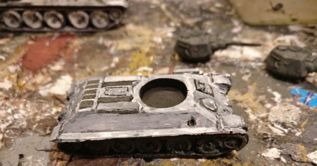 Dieses Foto zeigt den Resin T-34/76 nach dem Auftrag von mehreren Schichten weißer Lasuren. Ähnlich der Black-Lining-Technik spare ich tiefliegende Sektionen und Randpartien oder zB das Areal um die Fahrerluke vorn aus. Später würde ich diese mit Grüntönen noch weiter bearbeiten. Besonderheit: beim Lüftergitter am Heck ziehe ich die Stege zwischen den Gittersektionen mit weißer Farbe kräftig durch. So kommen die Gittertrenner besser hervor.